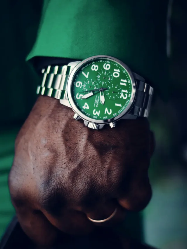 Close-up of a stylish green dial wristwatch on a fist, featuring a silver bracelet.