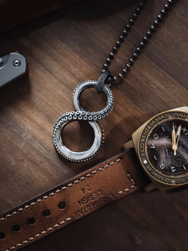 Close-up view of a unique necklace and stylish watch on a wooden desk.