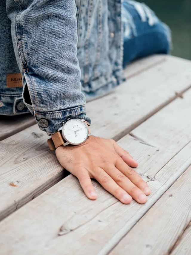 A casual look featuring a denim jacket and elegant wristwatch on a wooden deck.