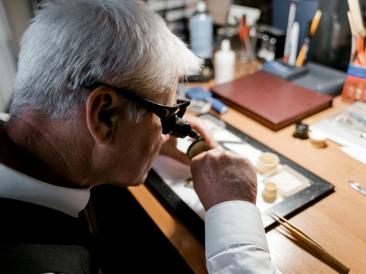 Senior watchmaker carefully examining a timepiece with a loupe in workshop.