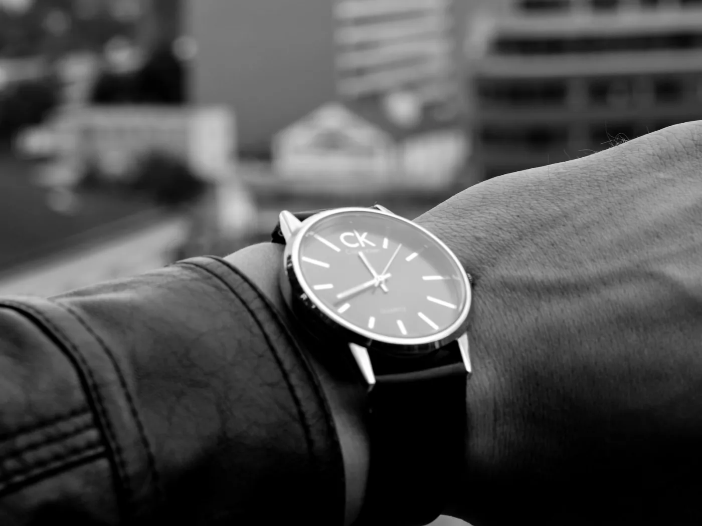 Stylish wristwatch on wrist in an urban outdoor setting, black and white.