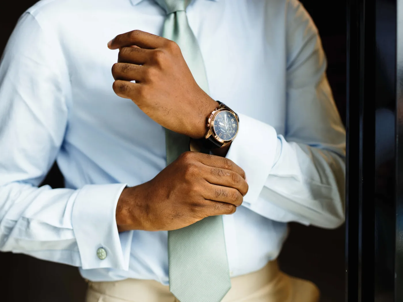 Close-up of a man adjusting his watch while wearing a stylish shirt and tie.