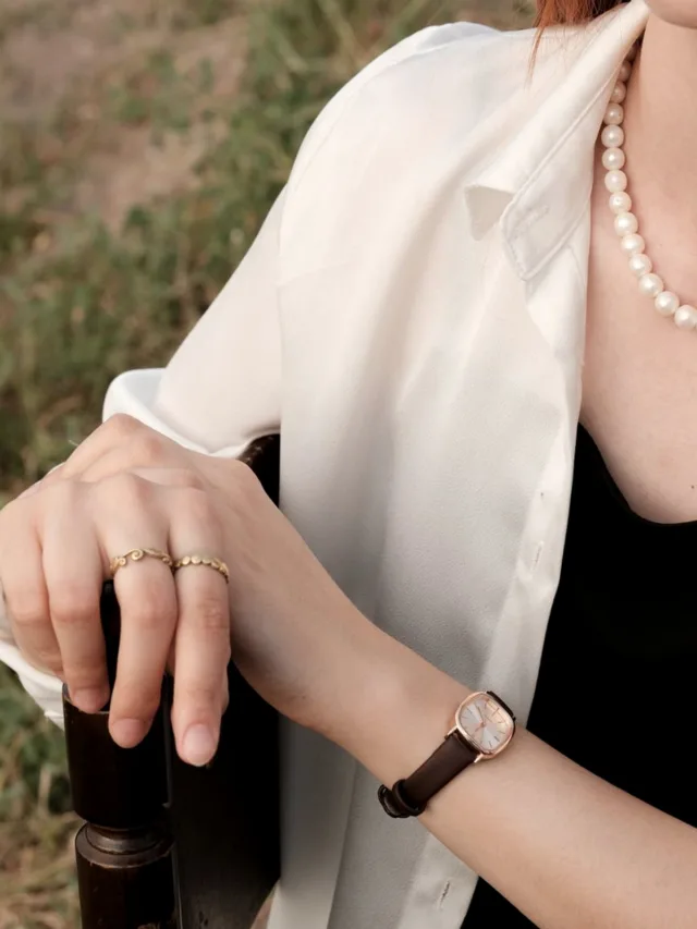 Chic close-up of a woman's hand with rings, watch, and pearl necklace outdoors.