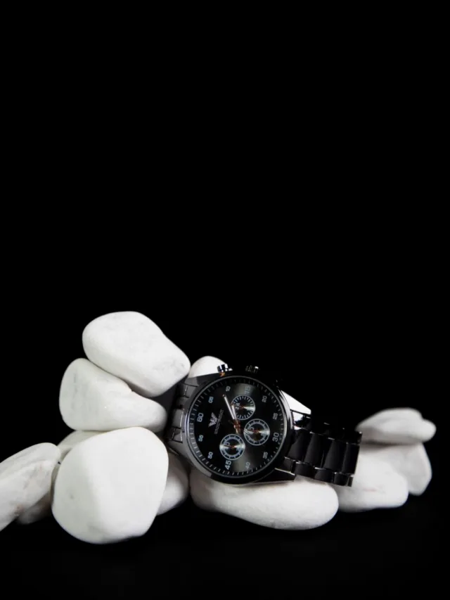 Sophisticated black watch displayed on smooth white stones for a stylish contrast.