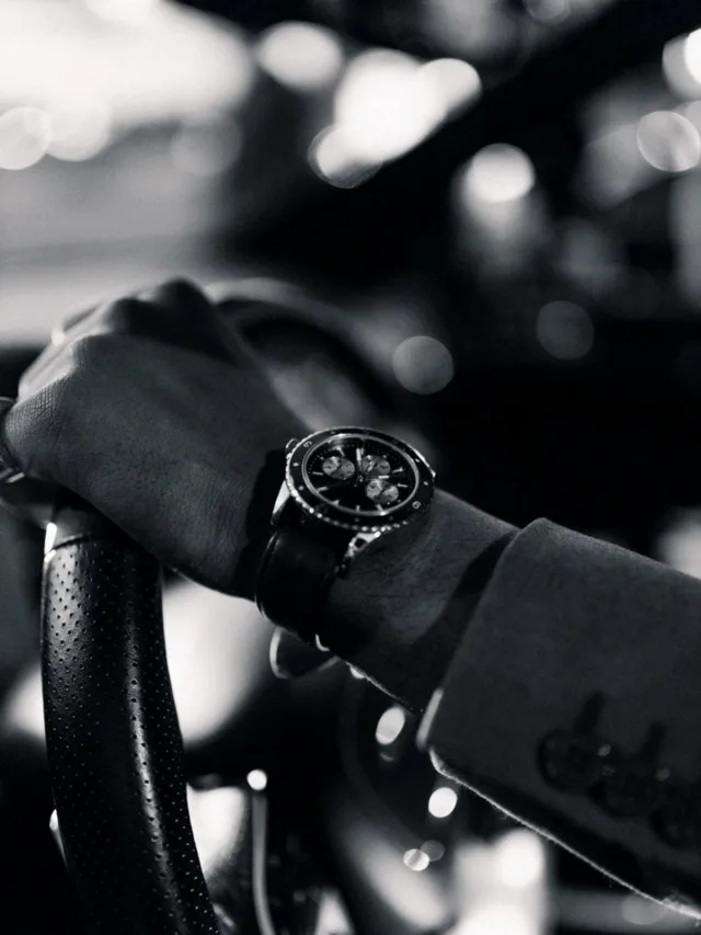 Monochrome close-up of a luxury wristwatch on a steering wheel, capturing elegance and detail.