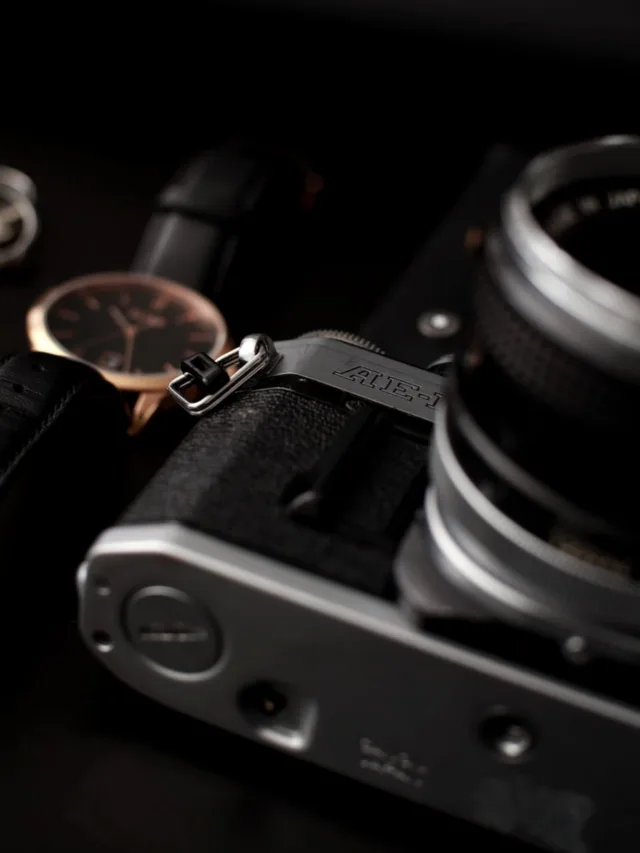 Detailed photo of a vintage camera and wristwatch on a dark surface, emphasizing elegance and nostalgia.